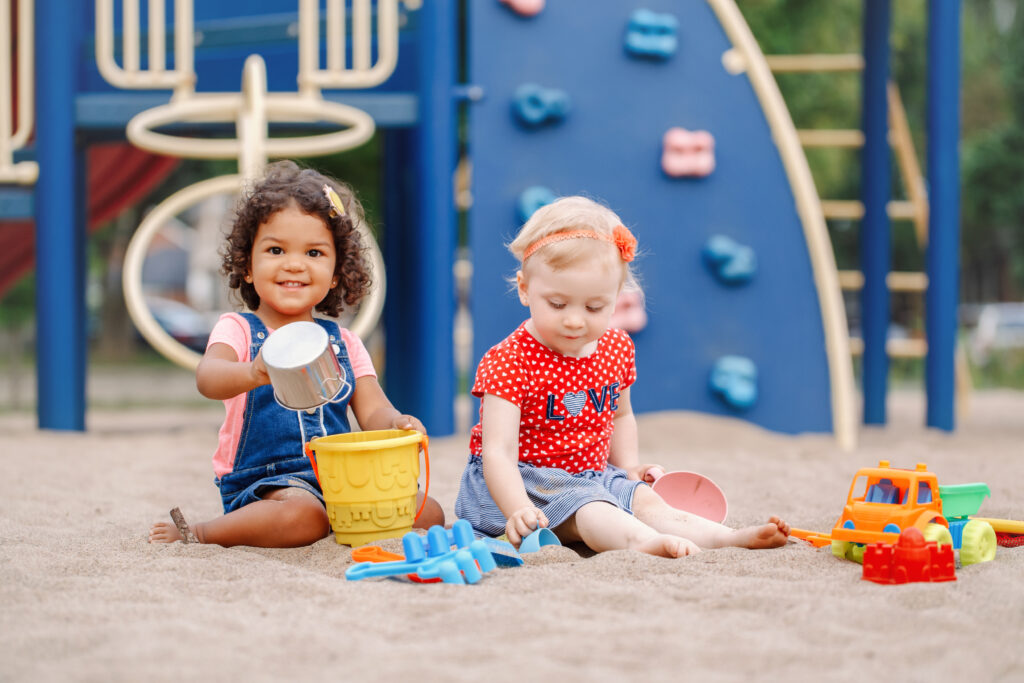 two toddlers sitting in sandbox playing with plastic colorful toys