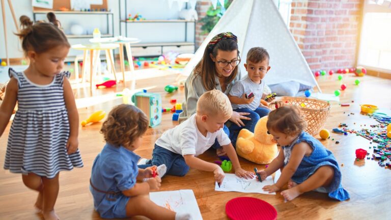 teacher and group of toddlers sitting on the floor drawing at daycare