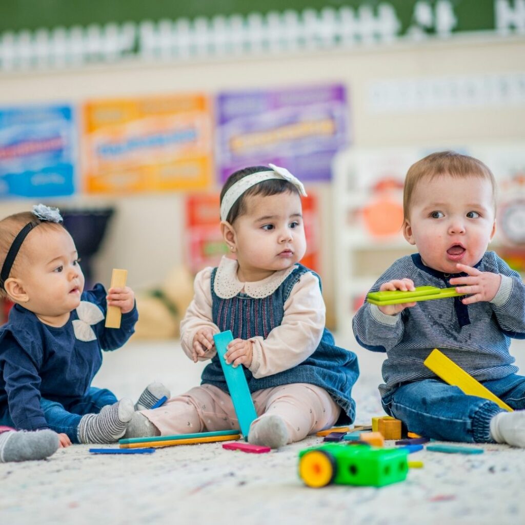 three babies sitting on floor with toys
