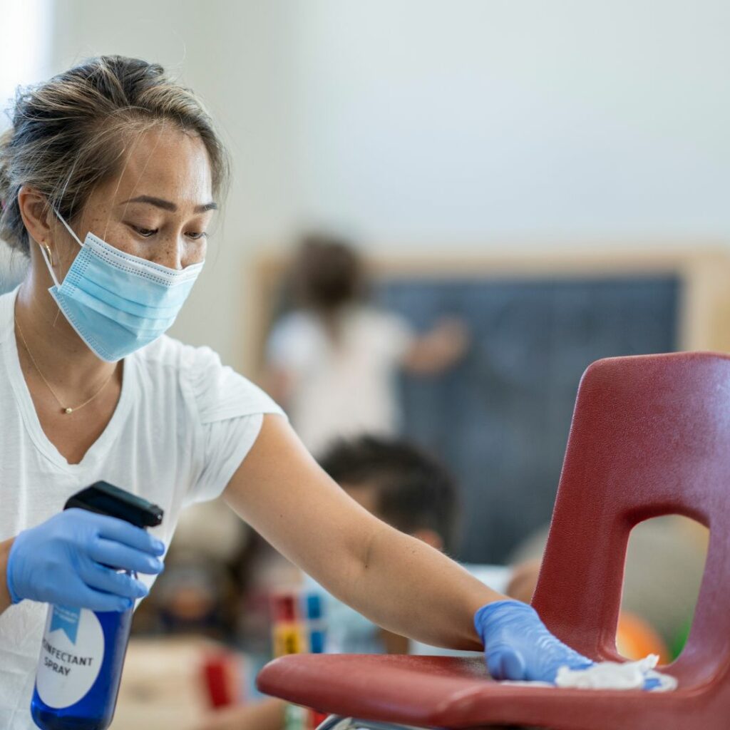 Woman wearing a mask, cleaning a classroom chair.