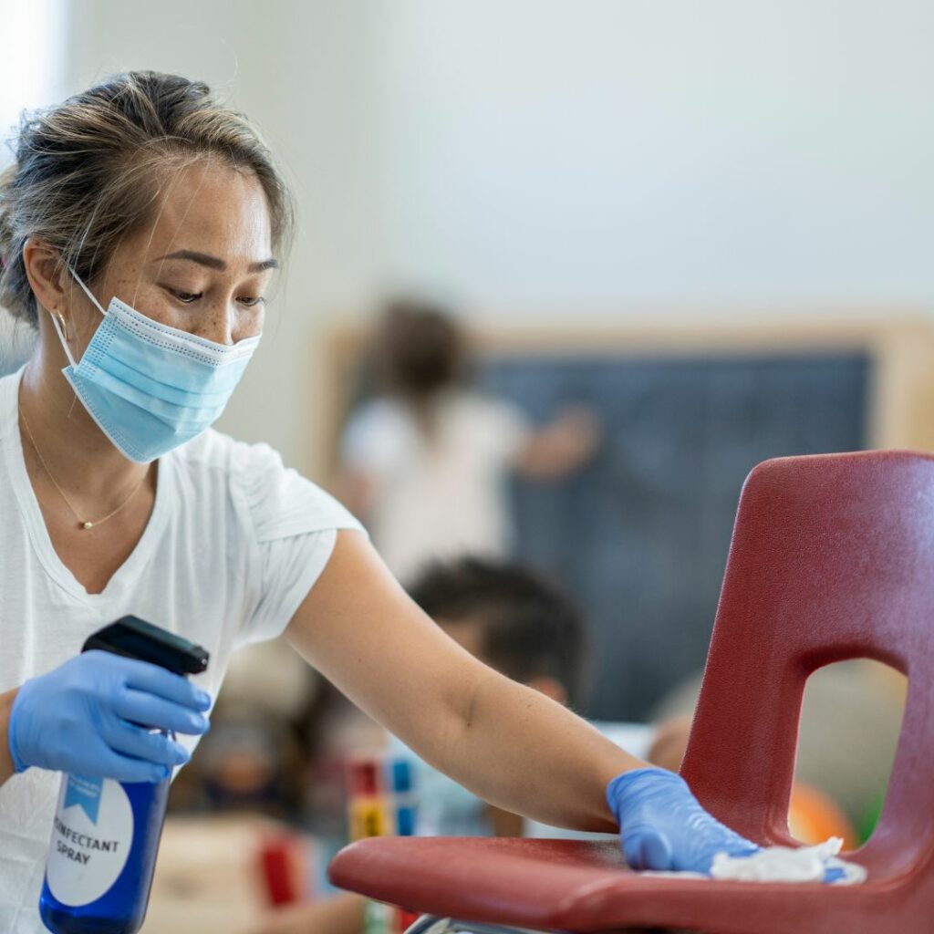 Woman wearing a mask, cleaning a classroom chair. 