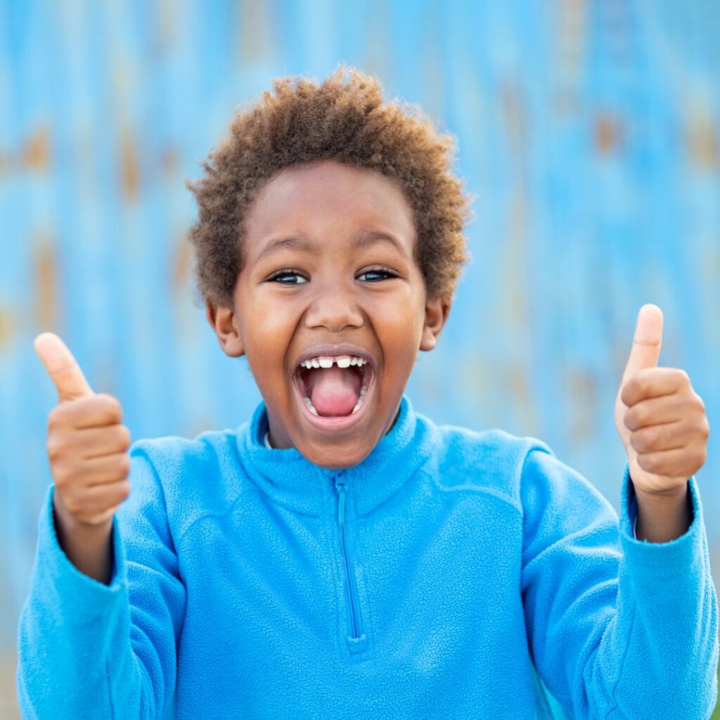 Young boy smiling and giving two thumbs up.