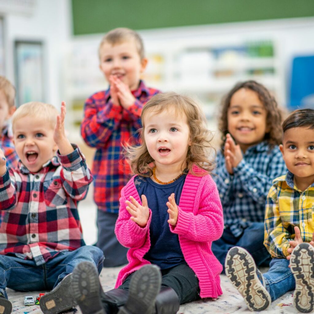 Pre-kindergarten-aged children clapping and looking happy. 